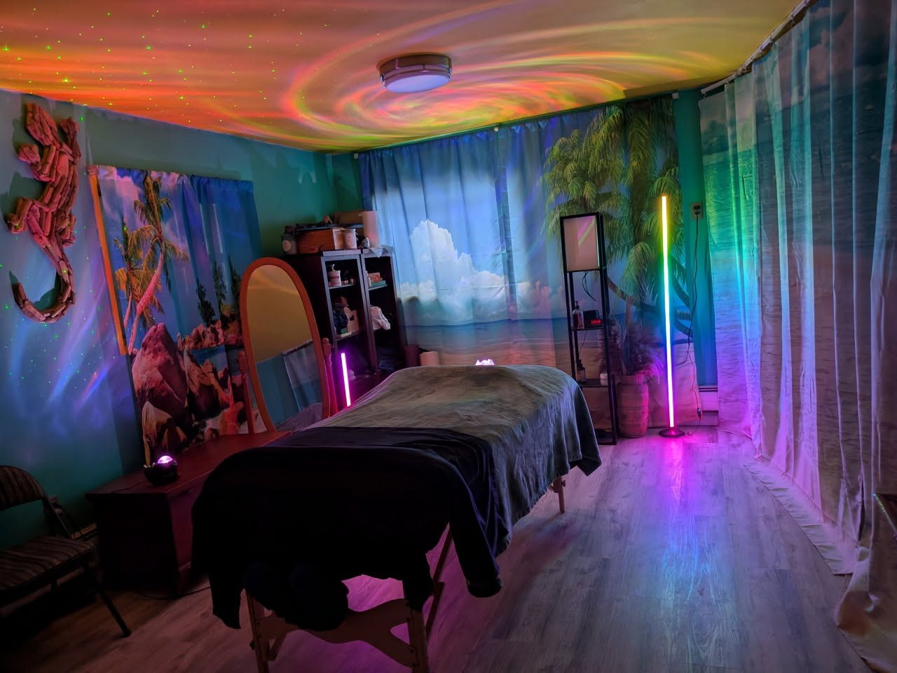 Kara's treatment room, lit by an aurora projector, with the massage table made up and tropical wall murals