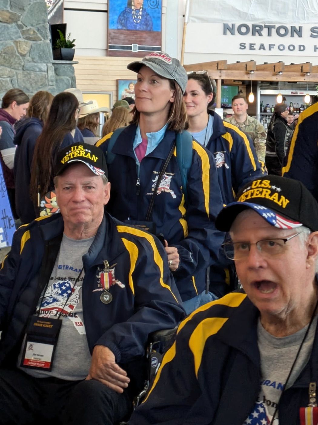 Two Veterans in Honor Flight jackets and U.S. Veteran caps in the airport
